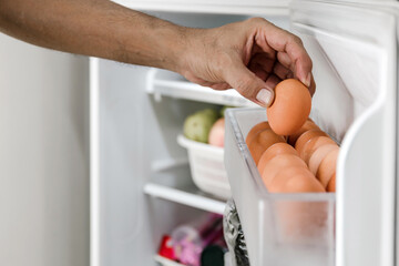 Closeup human hands put chicken eggs in the egg-laying compartment in the refrigerator