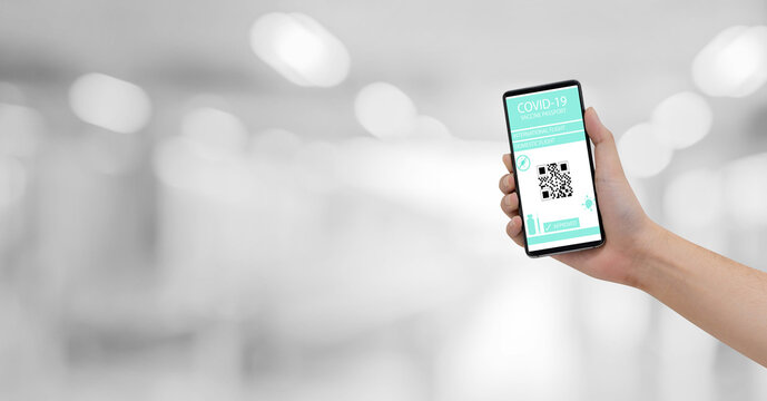 close up man hand hold smartphone to show vaccine passport of covid-19 isolated on blur airport background for travel concept