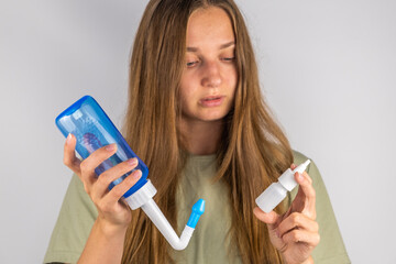 Girl holding a spray and a bottle for washing the nose in her hands - obrazy, fototapety, plakaty