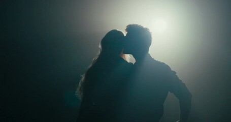 Dance of experienced partners in dark studio shadow of figure scene lit by lamp handsome man spins girl performing pirouettes several times in row tilts her down to first floor couple hugs