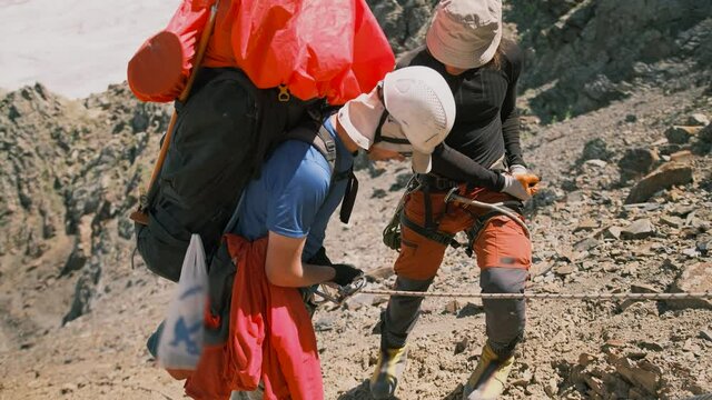 A mountaineering instructor teaches a tourist how to use the Eight Descent Device on a descent on a difficult mountain section. Two men prepare to use safety device and rope in the mountains