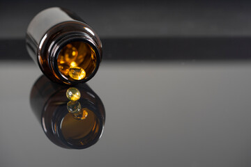 The tablets lie on a mirrored black background, reflect in it. Dark bottle with medicine out of...