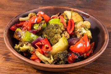 Cooked vegetables baked in the oven - broccoli, tomatoes, onions and zucchini with peppers in a plate on the table, close-up