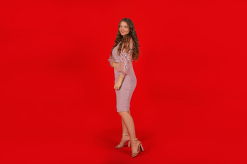 Fototapeta na wymiar a young elegant tall beautiful brown-haired girl with long hair in a pink festive dress on a red background
