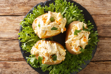 Baked potatoes with coronation chicken salad is a combination of cold cooked chicken meat, herbs and spices, and a creamy mayonnaise sauce closeup in the slate dish on the table. Horizontal top view