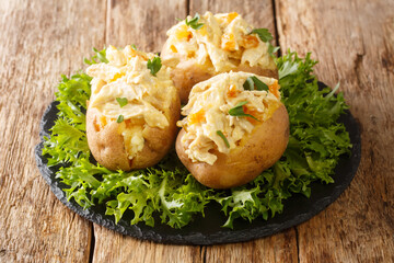 English food baked potatoes topped with coronation chicken salad with spices and dried apricots close-up on a slate board on the table. horizontal