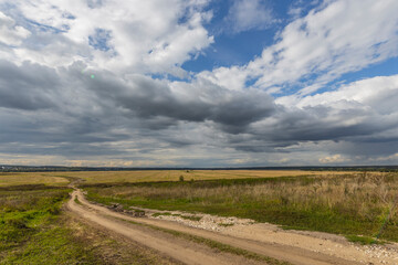 Road through fields. Country road in summer field and clouds on blue sky.
