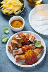 Currywurst or german traditional sausages served with tomato sauce, curry and fries, vertical shot on a blue stone background