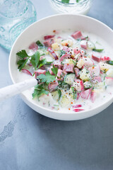 Cold soup okroshka with beef meat, potato, vegetables and kefir served in a white bowl, vertical shot on a grey concrete background