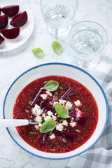 Plate of beetroot and quinoa soup topped with bryndza, vertical shot on a grey marble background, elevated view