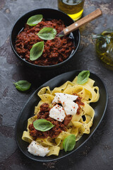 Italian pappardelle with bolognese sauce, mozzarella and fresh green basil, vertical shot on a brown stone background, selective focus