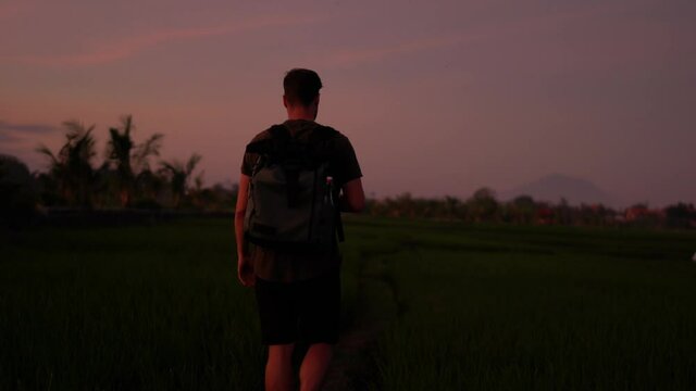 Video of caucasian male traveler with backpack using smartphone camera for making picture and shooting content for sharing in social networks during evening dusk on tropical destination
