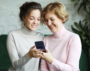 Fototapeta premium Family, people and technology concept: Aged woman and her adult daughter using smartphone at home