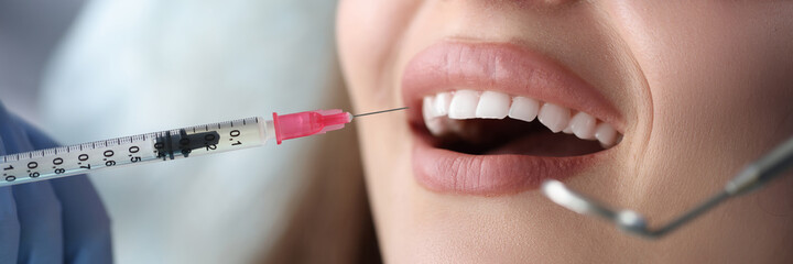 Fototapeta premium Portrait of young female patient sitting in dentist chair with mouth open and receiving an injection of anesthetic