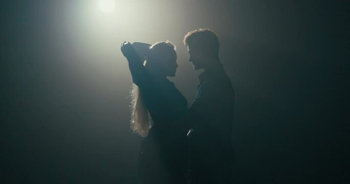 Shot of blurred figures dancing two partners on a dark stage illuminated by a single light, a couple in love focused on their movements, practicing choreography