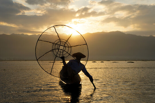 silhouette of local fisherman using coop to catching in inle lake at sunrise