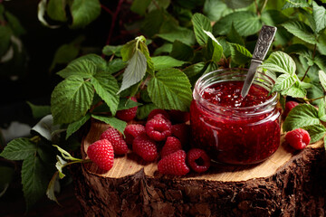 Jar of raspberry jam and fresh berries with leaves.