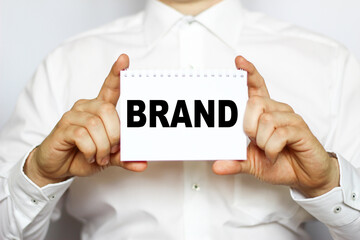 A businessman in a white shirt shows a business card with text BRAND, copy space, business concept
