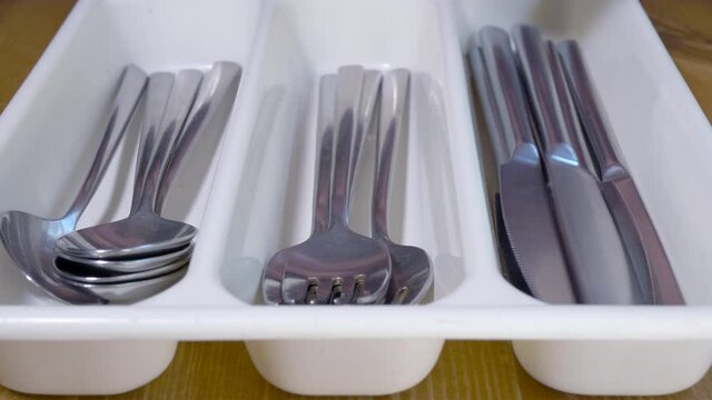 Closeup POV shot of hands quickly placing washed up steel knives, forks and spoons into their respective compartments in a plastic cutlery tray.