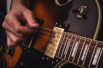 Person plucking the strings of an electric guitar with a pick. Selective focus. Copy space. - obrazy, fototapety, plakaty