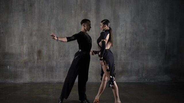 The young active millennial dance ballroom couple in black dress dancing in sensual pose over studio background. Professional dancers dancing latino. Hobby dance concept. Human emotions, love passion