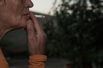 Detalle de mujer fumando tabaco con manchas en la piel y envejecida prematuramente a causa del tabaco aspirando el cigarro.  - obrazy, fototapety, plakaty