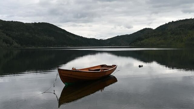 An empty wooden boat at the lake Fitjadalsvatnet, Norway. The hills in the background and the boat reflect in the lake's dark water.