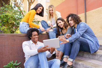 Multi-ethnic group of young people looking at a digital tablet outdoors in urban background.