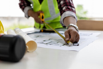 Obraz premium The male architect uses a tape measure to measure the house designs, he is checking the house plans that he has designed before sending it to the customers, he designs the house and the interior.