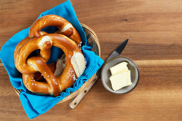Pretzels in a basket with a blue napkin and butter on a rustic wooden table. Top view and copy space.