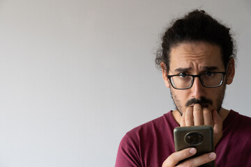 Close up with copy space of anxious man with smartphone biting his nails and looking at camera