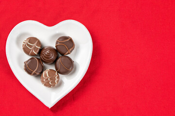 Chocolate praline on a heart-shaped plate on a red background, top view , copy space, chocolates for Valentines Day.