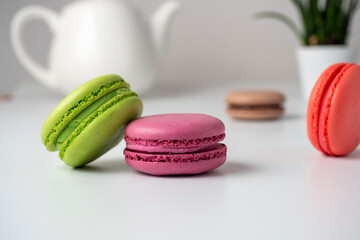 Colorful delicious macaroons lie on a white table. In the background is a white teapot and a flower