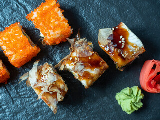 food composition with sushi rolls. A variety of sushi on a black plate, next to pickled ginger and wasabi. Top view, flat lay