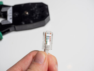 a man is holding a communication cable for connecting the Internet. In the background, cable crimping pliers