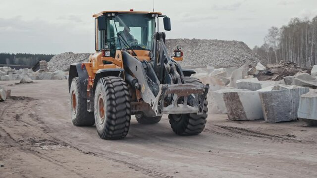 Handheld tracking of unrecognizable worker driving wheel loader along road in granite quarry