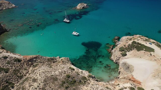 Aerial drone video of beautiful scenic rocky cove and beach of Tsigrado with caves and crystal clear emerald sea, Milos island, Cyclades, Greece