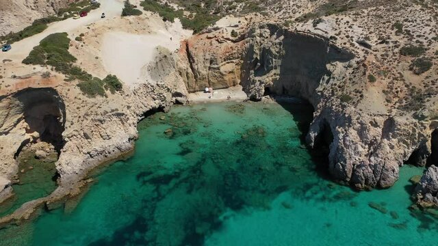 Aerial drone video of beautiful scenic rocky cove and beach of Tsigrado with caves and crystal clear emerald sea, Milos island, Cyclades, Greece