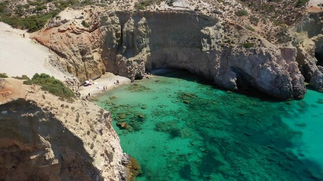Aerial drone video of beautiful scenic rocky cove and beach of Tsigrado with caves and crystal clear emerald sea, Milos island, Cyclades, Greece