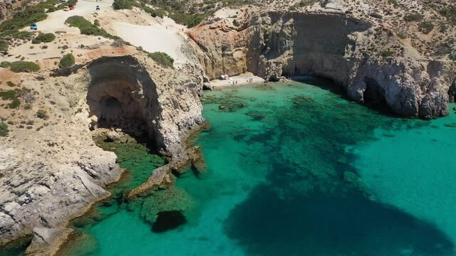 Aerial drone video of beautiful scenic rocky cove and beach of Tsigrado with caves and crystal clear emerald sea, Milos island, Cyclades, Greece