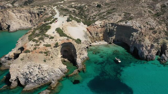 Aerial drone video of beautiful scenic rocky cove and beach of Tsigrado with caves and crystal clear emerald sea, Milos island, Cyclades, Greece