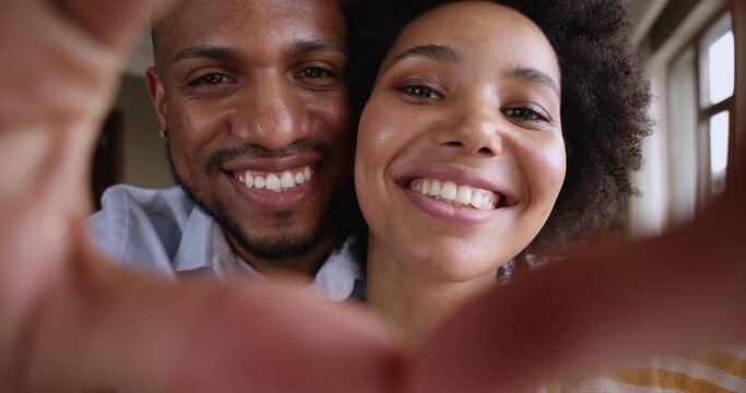 Close up portrait of happy faces of African couple looking through joined fingers making heart shape. St Valentines Day, romantic relations, just married, vloggers record video on camera, love concept