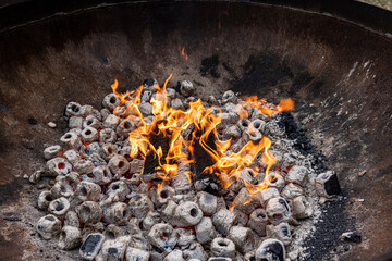 Burning charcoal with some wood in a large rustic metal pot