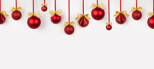 Christmas banner in simple minimal style - bright red balls with golden bows hanging on ribbon in row as pattern on soft light white wall. Background for design of website, header, card, brochure.