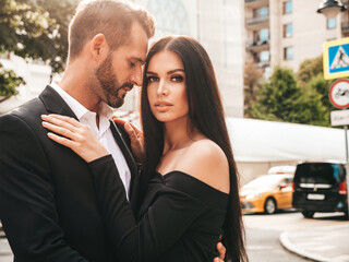 Beautiful fashion woman and her handsome elegant boyfriend in suit. Sexy brunette model in black evening dress. Fashionable couple posing in the street in Europe. Brutal man and his female outdoors