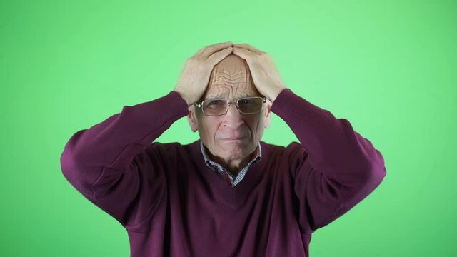 Sick old man with headache holding head with hands in studio with green screen background for chromakey effect