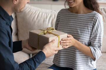 Close up caring young man giving wrapped carboard box to wife, congratulating with happy birthday or special event. Loving sincere millennial generation family couple celebrating wedding anniversary.