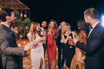 Group of beautiful people in formalwear communicating and smiling while spending time on luxury...