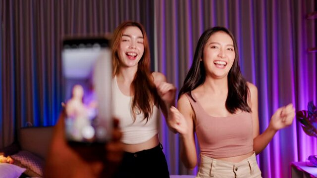 Asian and mixed race  female influencer shooting dance video for social media on mobile phone, having fun at home. To share video to social media application..