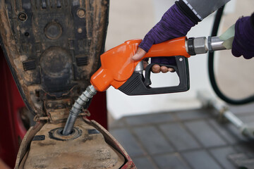 Closeup of hand holds the orange petrol pump filling nozzle to fill fuel into motorcycle. Refueling...